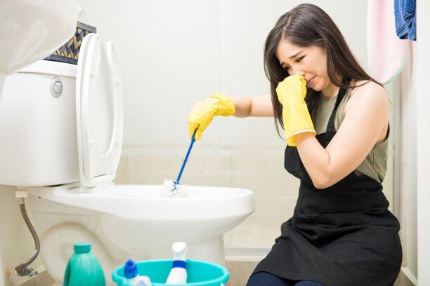 STINKY PROBLEMS: A lady that is cleaning the toilet and trying to cover her noise from the smell
