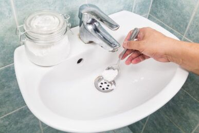 A person pouring a caustic soda solution into a clogged drain to clear the blockage effectively.