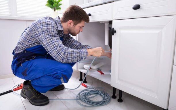 Plumber performing professional drain cleaning in a residential kitchen.