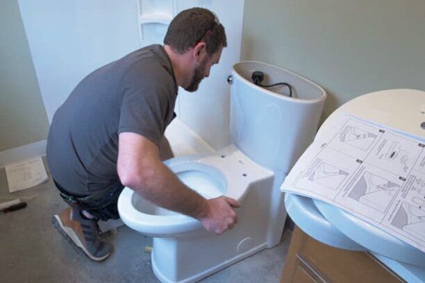 Plumber explaining the charge to install a toilet in a modern bathroom setting.
