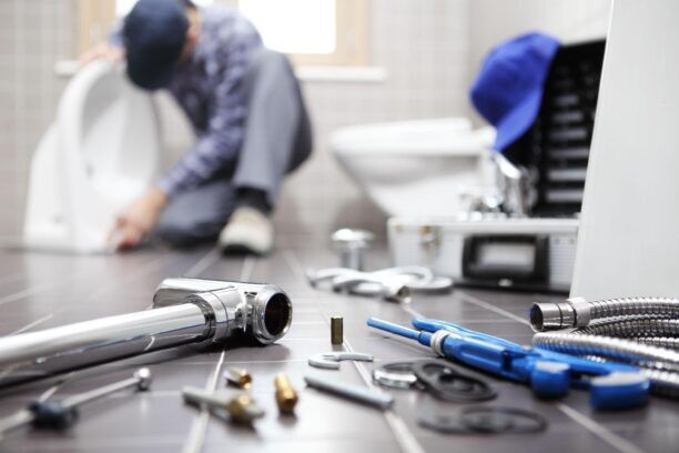 Technician repairing a pipe under a kitchen sink, representing hands-on work in the Plumbing Industry.