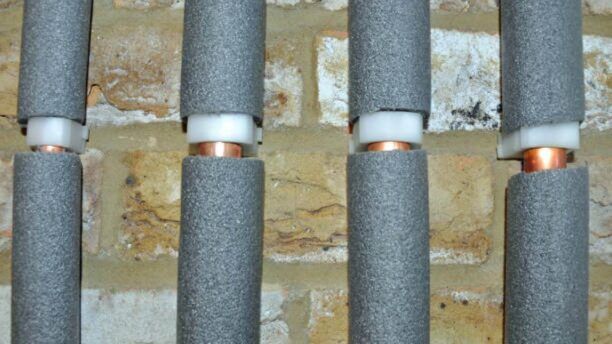 Worn-out pipe insulation on a basement pipe showing visible damage and condensation.